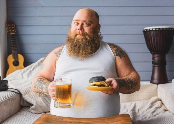 pretili muškarac sjedi s pivom i hamburgerom