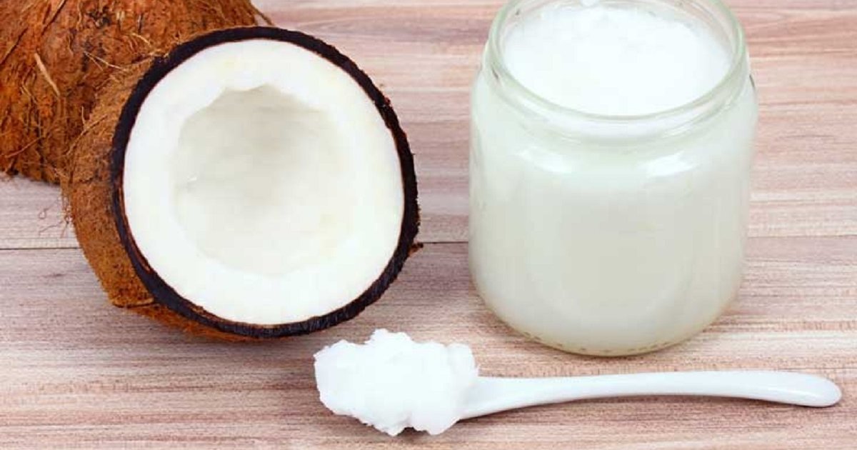 Bijelo kokosovo ulje na žličici i u stalenoj ambalaži na drvenom stolu pored polovice kokosa.