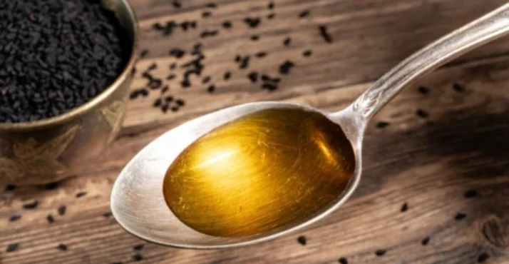 Ulje crnog kima u staklenki pored crnih sjemenki na bijeloj pozadini.