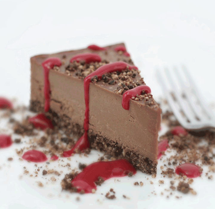 Tamna čokoladna tofu torta prelivena crvenim preljevom na bijelom tanjuru.