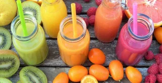 Narančasti, zeleni, rozi smoothie okruženi voćem na drvenom stolu