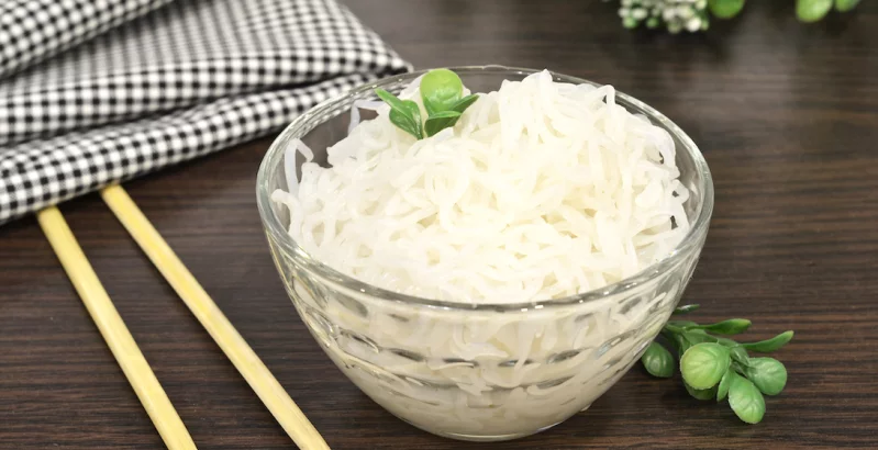 Bijela tjestenina pomiješana s povrćem na tavi.