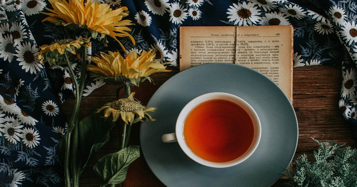 Šalica čaja na knjizi pored cvijeta.